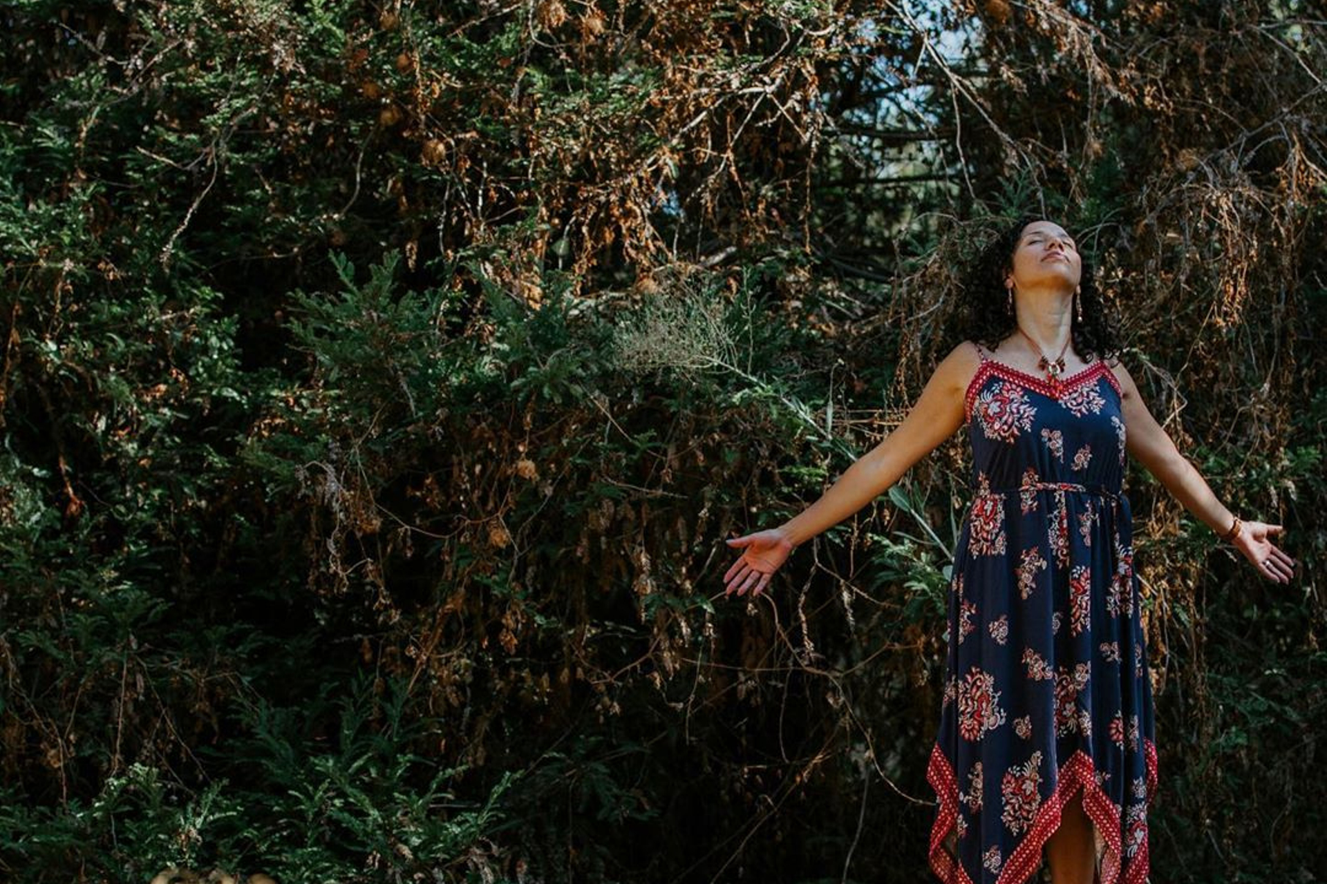 Natalie Gutierrez stands on a tree stump with arms outstretched in a forest