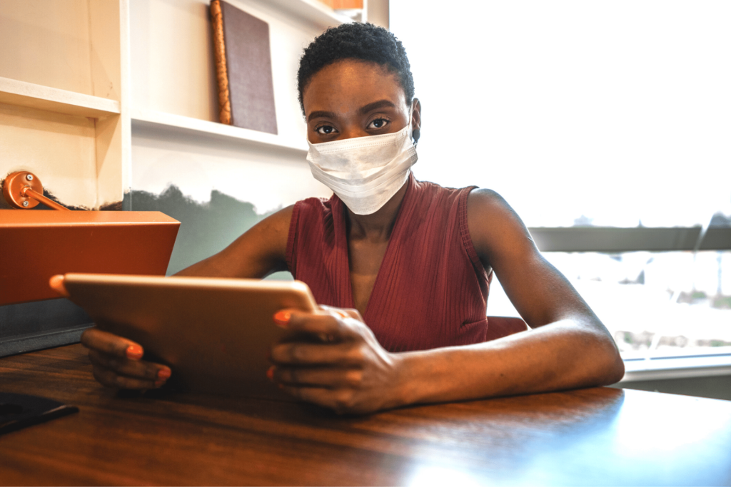Black woman wearing a face mask and holding a tablet