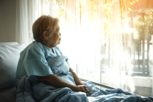 An elder woman sitting in bed looking out of the window.