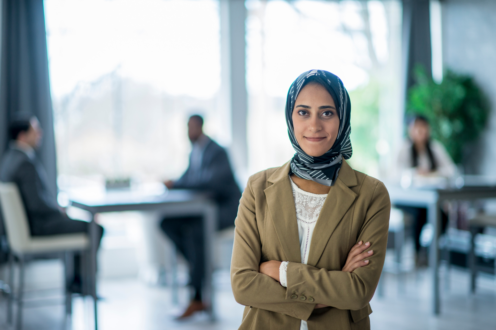 Woman in brown blazer and blue hijab stands in office