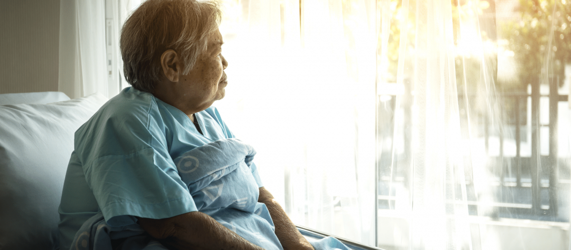 An elder woman sitting in bed looking out of the window.