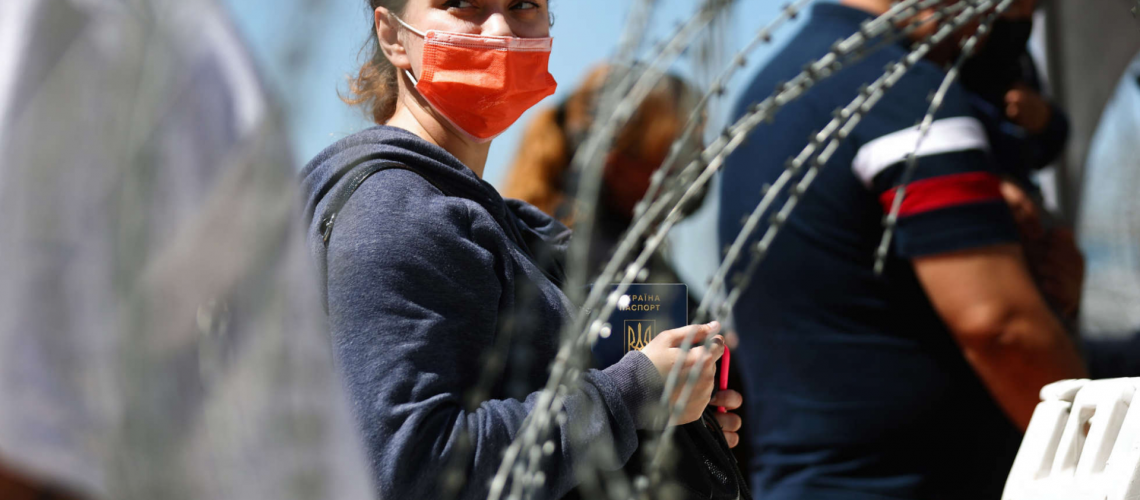 Person with red mask in front of barbed wire fence_Truthout