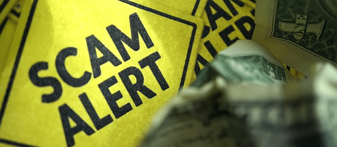 Yellow hazard sign with "scam alert" written on it.